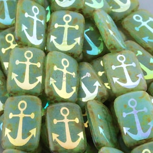 May include: A close-up of a pile of green glass beads with an anchor design. The beads are iridescent and have a rustic, aged look.