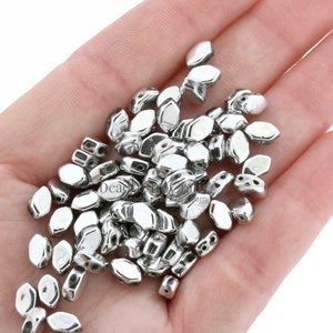 May include: A pile of silver-toned metal beads with a faceted oval shape. Each bead has two holes for stringing.