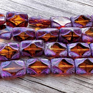 May include: Rows of iridescent purple and gold rectangular beads. Each bead has a geometric design with a central gold-colored core. The beads are arranged on a wooden surface, with the text "beadBistroCrafts" visible.