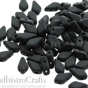 May include: A pile of black matte glass beads in a teardrop shape. The beads have two holes for stringing.