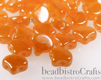 May include: A close-up of a pile of small, orange, iridescent glass beads. The beads are shaped like a crescent moon and have a smooth, shiny finish.