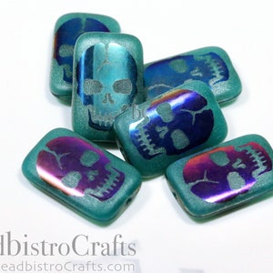 May include: Teal green glass beads with iridescent skull designs. The beads are rectangular in shape and have a textured surface.