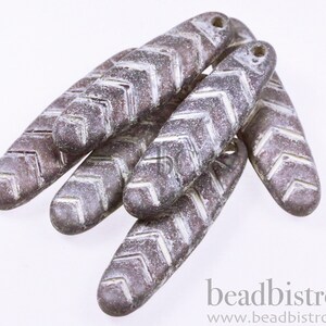 May include: A group of six grey and white ceramic beads with a chevron pattern. The beads are oval shaped and have a hole at the top for stringing.