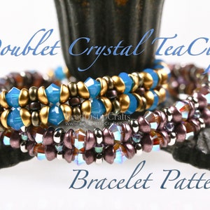 May include: Three beaded bracelets in a blue, gold, and purple color scheme. The bracelets are stacked on top of each other and the text "Doublet Crystal Tea Cup Bracelet Pattern" is visible below the bracelets.