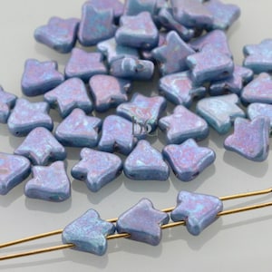 May include: A collection of iridescent blue-purple star-shaped beads. Some beads are strung on gold-colored wire. The beads have a textured surface and are scattered across a light background. These beads are suitable for jewelry making.