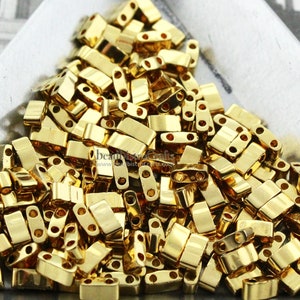 May include: A pile of gold-colored metal beads with two holes in each bead. The beads are rectangular in shape and have a shiny finish.