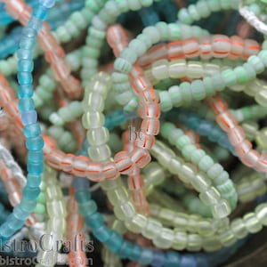 May include: A close-up of a selection of glass beads in shades of blue, green, and peach. The beads are small and round, and they are arranged in a random pattern. The beads are ideal for jewellery making or other craft projects.
