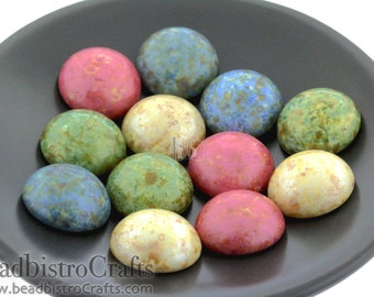 May include: A collection of 10 round ceramic cabochons in various colors and patterns, including blue, green, red, and cream. The cabochons are displayed on a black plate.