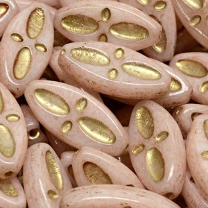 Peut inclure: Gros plan sur un groupe de perles en verre de forme ovale, de couleur rose clair et avec des accents dor&eacute;s. Les perles ont une surface textur&eacute;e et sont parfaites pour la fabrication de bijoux.
