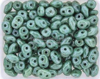 May include: A collection of green, double-holed beads. The beads have a speckled appearance and are oval or rounded in shape. The beads are in a white container. The beads are for jewelry making.