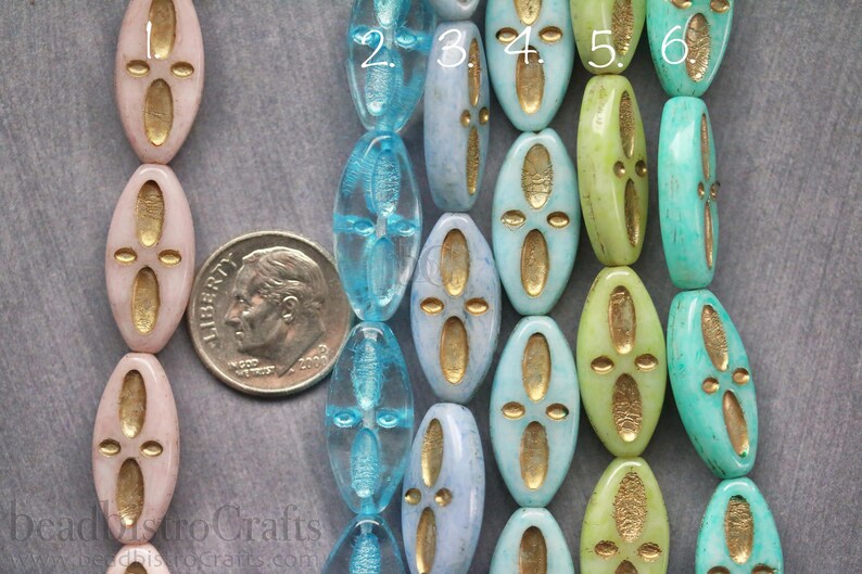 Peut inclure: Gros plan sur dix perles ovales en verre avec des accents dor&eacute;s. Les perles sont dispos&eacute;es en rang&eacute;e, avec les chiffres 2 &agrave; 6 visibles sur le dessus des perles. Les perles sont bleu clair, turquoise et vertes.