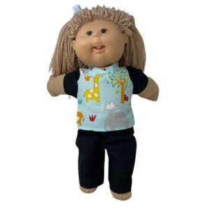 May include: A doll with light brown hair and a blue bow. The doll is wearing a black shirt with a light blue animal print top and black pants. The animal print includes a giraffe, tree, and elephant.