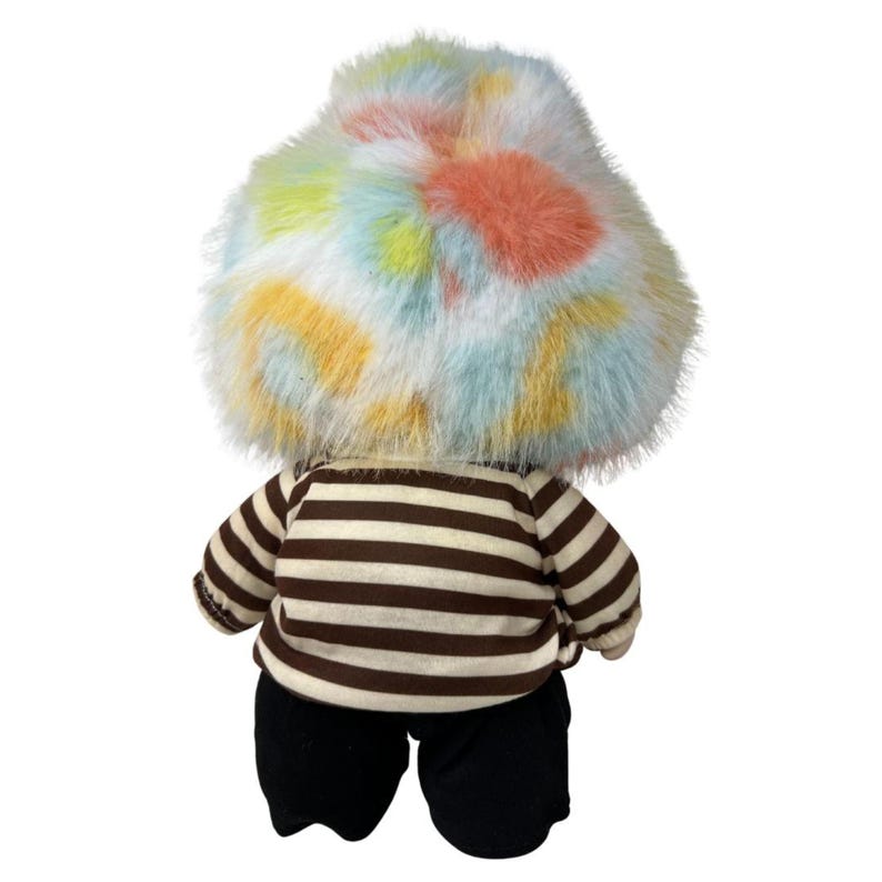 May include: A plush toy with a colorful, fluffy head in shades of blue, yellow, orange, and pink. The toy wears a brown and white striped shirt and black pants. The toy is viewed from the back.