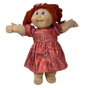 May include: A vintage doll with red yarn hair and blue eyes. The doll is wearing a red dress with a swirl pattern. The doll has its arms outstretched.