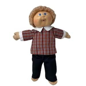 May include: A vintage Cabbage Patch Kid doll with a tan face, blue eyes, and light brown yarn hair. The doll is wearing a red and black plaid shirt with a white collar and cuffs, and black pants. The doll's arms are outstretched.