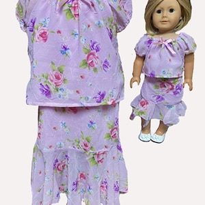 May include: A lavender doll outfit featuring a floral print with pink and purple roses, green leaves, and blue accents. The outfit includes a top with a bow and a skirt with a ruffled hem. A matching outfit is on a doll.