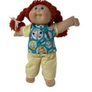 May include: A vintage doll with red braided hair and blue eyes. The doll is wearing a teal top with a circular pattern and yellow pants. The doll's arms are outstretched.
