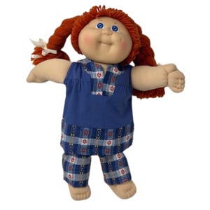 May include: A vintage doll with red yarn pigtails and blue eyes. The doll is wearing a blue top and matching plaid pants with red and white accents. The doll has a soft, fabric body and is standing.