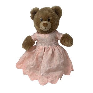 May include: A brown teddy bear wearing a pink dress with a lace overlay. The dress has short sleeves and a flared skirt. The bear has a brown nose and eyes.