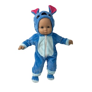 May include: A doll wearing a blue plush costume with a hood featuring pink-lined ears. The costume has a light blue belly and a zipper closure. The doll's arms are outstretched, and it is standing against a white background.