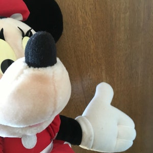 Peut inclure: Un jouet en peluche de Minnie Mouse portant une robe rouge &agrave; pois blancs et un n&oelig;ud noir. Le jouet a un gant blanc sur sa main droite.