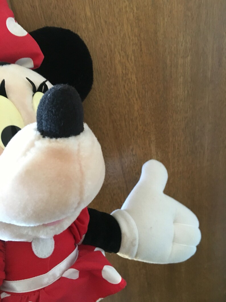 Peut inclure: Un jouet en peluche de Minnie Mouse portant une robe rouge &agrave; pois blancs et un n&oelig;ud noir. Le jouet a un gant blanc sur sa main droite.
