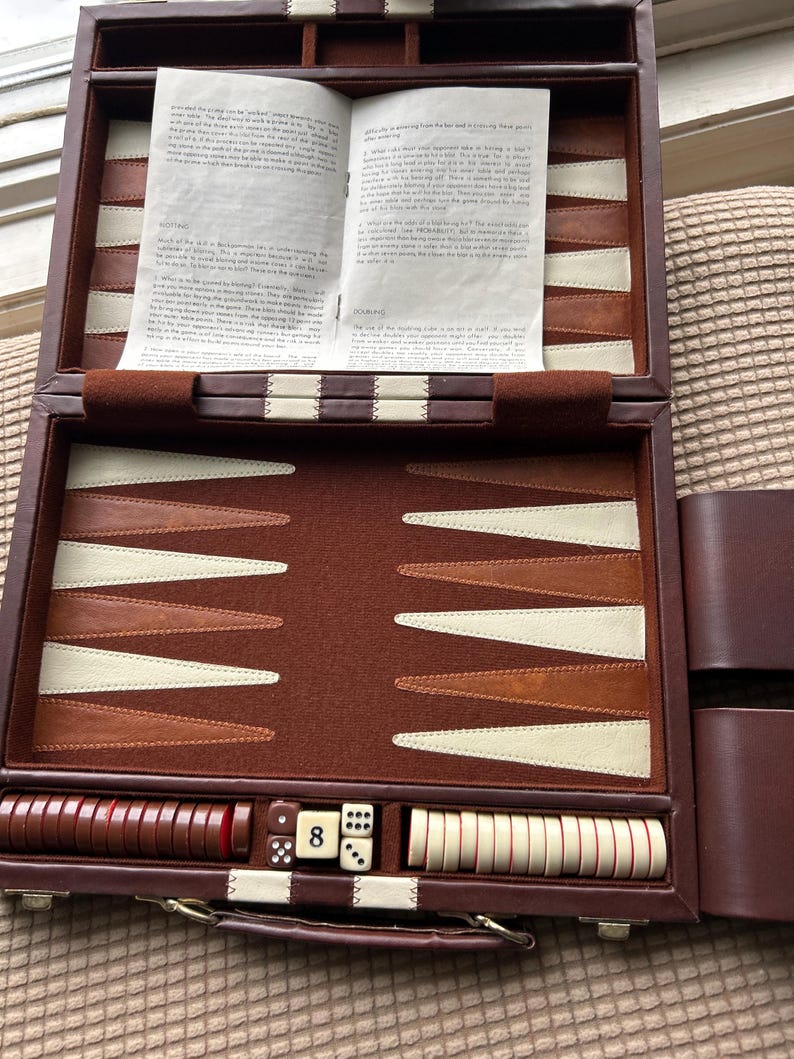 May include: Open brown leather backgammon set with ivory and brown playing pieces, dice, and a doubling cube showing the number 8. The game board is open, revealing the playing surface and instructions.