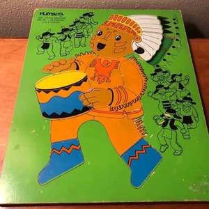 May include: A vintage Playskool wooden puzzle featuring a Native American man playing a drum. The puzzle is on a green background and includes the text "Ten Little Indians 300+ Pieces Ages 3 to 8 Years".