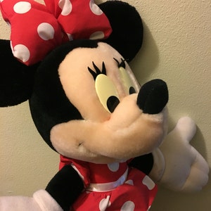 Peut inclure: Un jouet en peluche de Minnie Mouse portant une robe rouge &agrave; pois blancs et un n&oelig;ud rouge &agrave; pois blancs.
