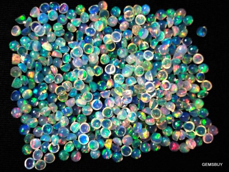 May include: A large group of iridescent opal cabochons in various shades of blue, green, and pink. The cabochons are round and have a smooth, polished surface.