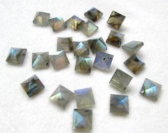 May include: A collection of 20 square-shaped labradorite gemstones with a pyramid-shaped top. The stones are a mix of gray, blue, and green with iridescent flashes.