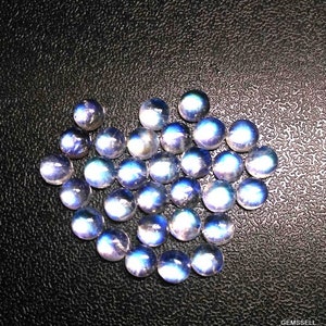 Puede incluir: Una colecci&oacute;n de cabujones de piedras preciosas iridiscentes azules y blancas. Los cabujones son redondos y tienen una superficie lisa y pulida.