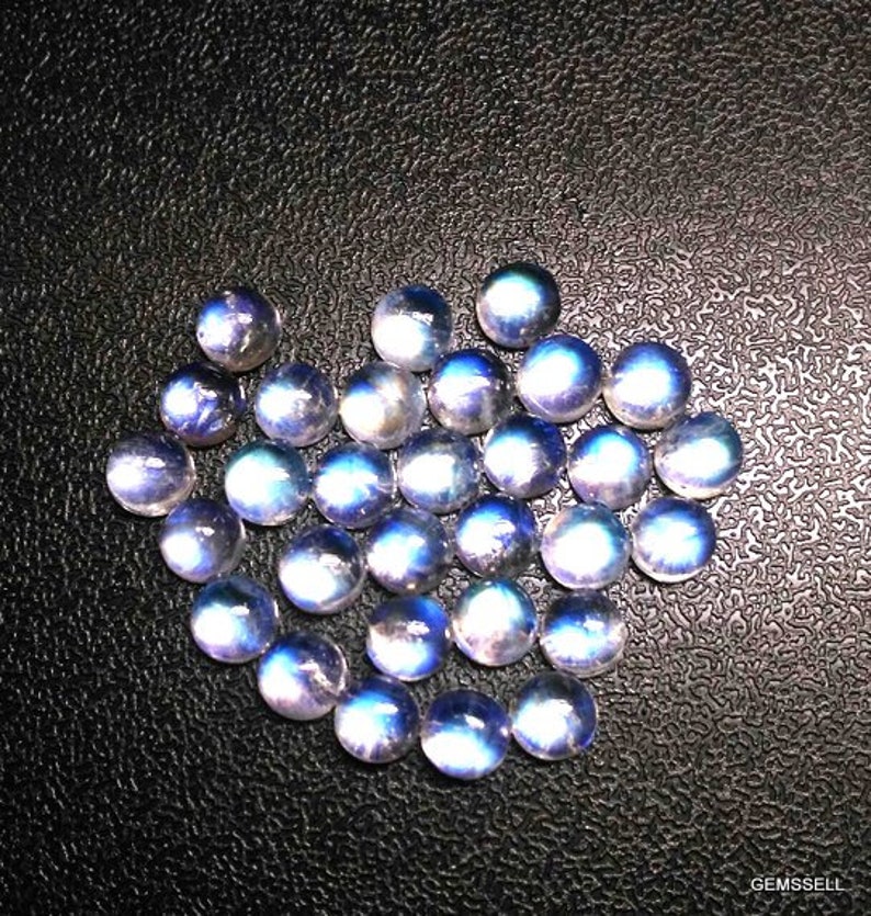 Puede incluir: Una colecci&oacute;n de cabujones de piedras preciosas iridiscentes azules y blancas. Los cabujones son redondos y tienen una superficie lisa y pulida.