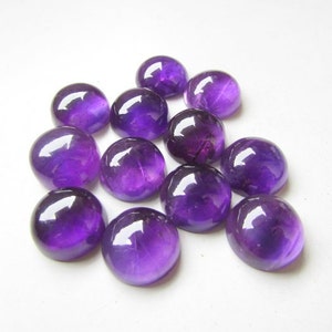 May include: A group of 12 round, purple amethyst cabochons. The cabochons are smooth and polished, with a slight variation in size and shape.
