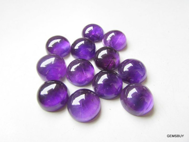 May include: A group of 12 round, purple amethyst cabochons. The cabochons are smooth and polished, with a slight variation in size and shape.
