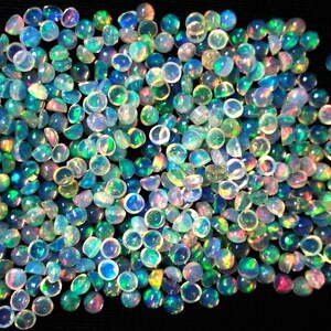 May include: A large pile of iridescent opal cabochons in various shades of blue, green, and white. The cabochons are round and have a smooth, polished surface.