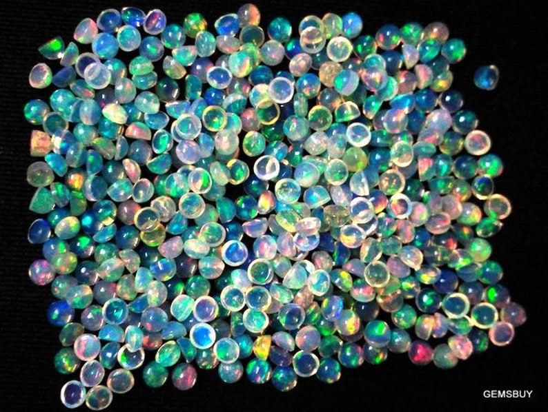 May include: A large pile of iridescent opal cabochons in various shades of blue, green, and white. The cabochons are round and have a smooth, polished surface.