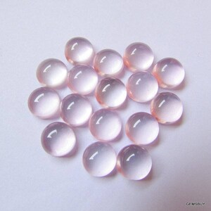 May include: A collection of 18 round, pale pink cabochon gemstones. The stones are smooth and polished, with a translucent appearance.