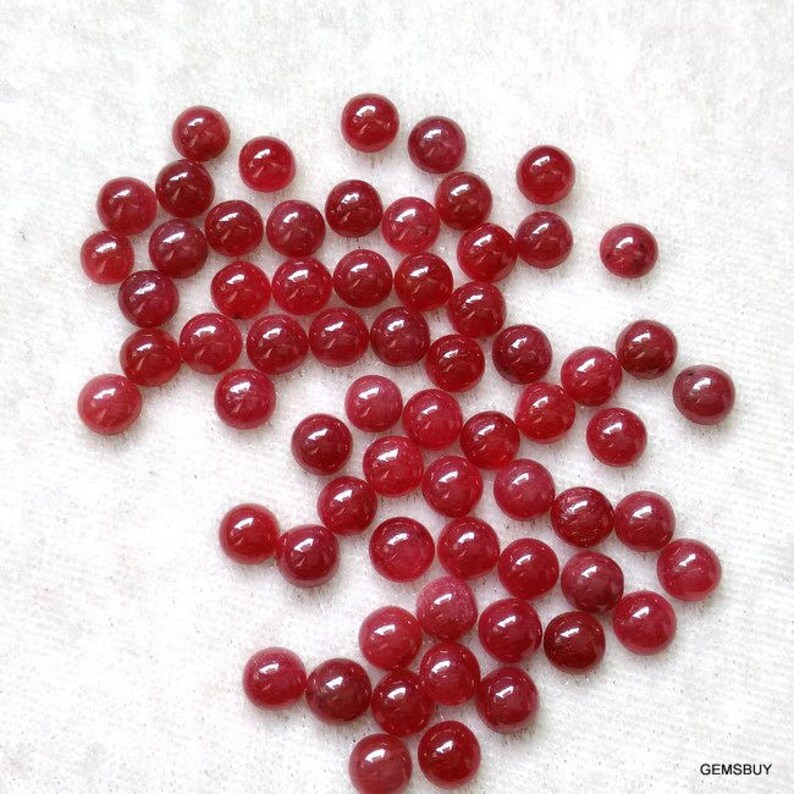 May include: A collection of 40 round, red ruby gemstones. The gemstones are smooth and polished, and they are all approximately the same size.