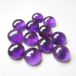 May include: A group of 12 round, purple amethyst cabochons. The cabochons are smooth and polished, with a slight variation in size and shape.