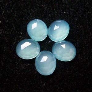 May include: Six smooth, light blue, oval-shaped gemstones on a black background.