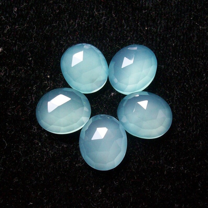 May include: Six smooth, light blue, oval-shaped gemstones on a black background.