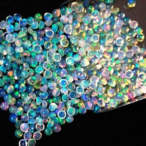 Op de afbeelding: Een stapel iriserende opaal cabochons in verschillende tinten blauw, groen en wit. De cabochons zijn rond en hebben een glad, gepolijst oppervlak.