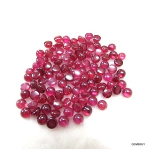May include: A pile of approximately 100 round, red ruby cabochons. The cabochons are about 4 mm in diameter and have a smooth, polished surface.
