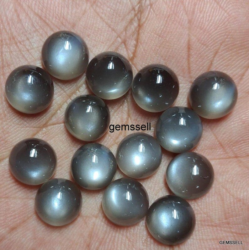 May include: A collection of 14 round, gray moonstone cabochons. The stones have a smooth, polished surface and a subtle shimmer.