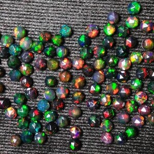 Puede incluir: Una colecci&oacute;n de piedras preciosas de &oacute;palo negro facetadas y sueltas. Los &oacute;palos son redondos y tienen una variedad de colores iridiscentes, incluyendo verde, azul, rojo y morado.