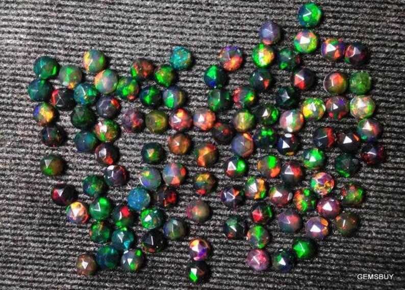 Puede incluir: Una colecci&oacute;n de piedras preciosas de &oacute;palo negro facetadas y sueltas. Los &oacute;palos son redondos y tienen una variedad de colores iridiscentes, incluyendo verde, azul, rojo y morado.