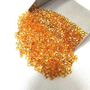May include: A large pile of small, round, orange-brown gemstones. The gemstones are loose and scattered on a white surface.