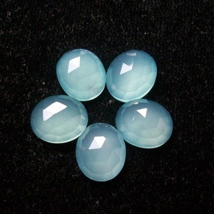 May include: Five light blue chalcedony gemstones arranged in a flower shape on a black background.