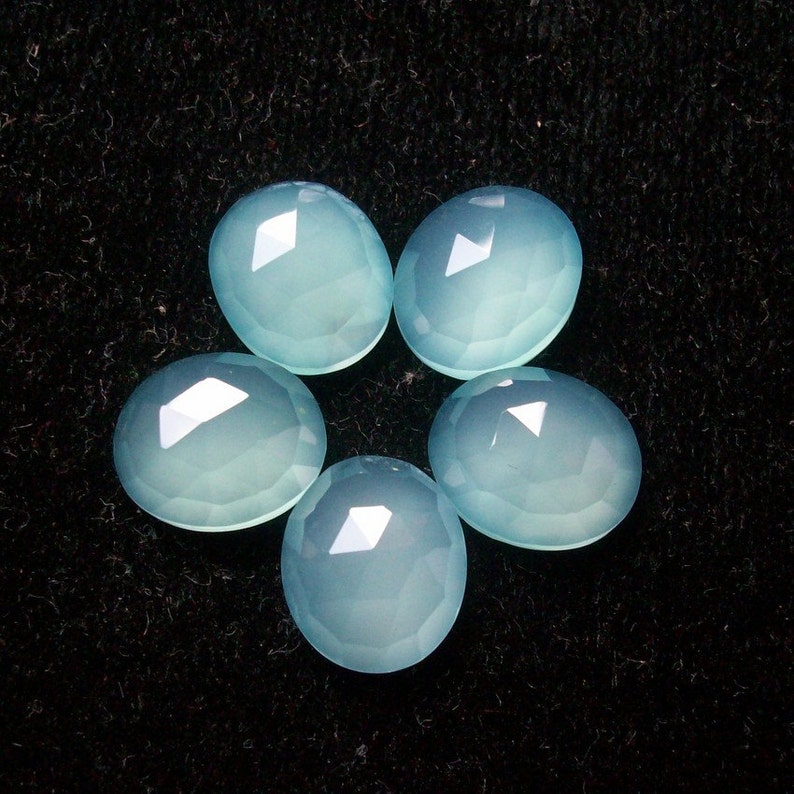May include: Five light blue chalcedony gemstones arranged in a flower shape on a black background.
